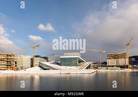 Oslo, Norvège, Mars 2018 : l'Opéra entouré par des grues. En face de la mer, ciel bleu avec des nuages blancs. La neige blanche sur le terrain. Banque D'Images