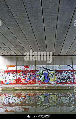 Le Graffiti sous un pont routier, se reflète dans l'eau calme du Grand Union Canal, Leighton Buzzard, Bedfordshire, Royaume-Uni. Banque D'Images