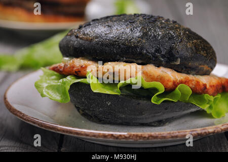 Hamburger fraîchement préparé avec le rouleau de couleur noire, les légumes et le saumon escalope. Gros plan sandwich fait maison Banque D'Images