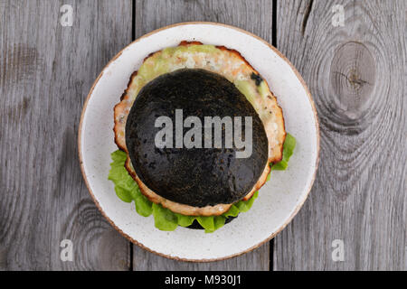 Hamburger fraîchement préparé avec le rouleau de couleur noire, les légumes et le saumon escalope. Sandwich fait maison, vue du dessus Banque D'Images