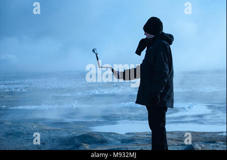 Namafjall champs géothermiques, de l'Islande - Mars 2016 : l'homme à prendre des photos avec l'appareil photo sur stick selfies, entouré par la vapeur, sulfureuse mudpots Banque D'Images