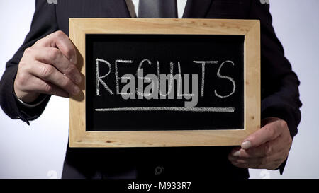 Résultats écrits sur tableau noir, l'homme en costume classique holding sign, business Banque D'Images