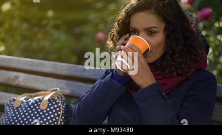 Attractive Woman talking on smartphone, de boire un café chaud à l'extérieur, jour frisquet Banque D'Images
