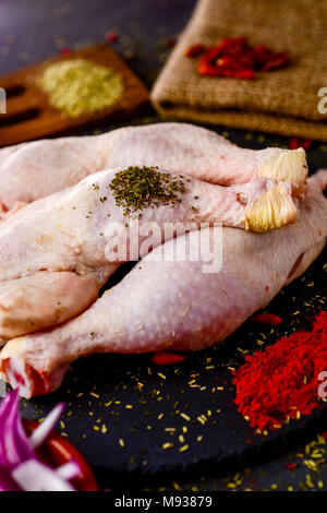 Libre de certaines matières les cuisses de poulet sur une plaque en ardoise, placé sur une table en bois rustique, saupoudrées d'épices différentes Banque D'Images