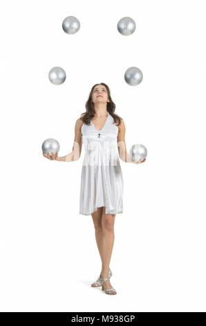 Une jeune femme artiste de cirque, jongle avec des balles en argent. Studio shot sur fond blanc, isolé de l'image. Banque D'Images