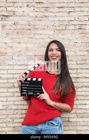 Jeune actrice brésilienne latina woman posing with movie clapper board souriant et regardant Banque D'Images