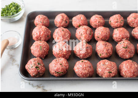 Boulettes de viande crus préparés et prêts à être cuits sur une feuille avec les assaisonnements sur le côté Banque D'Images