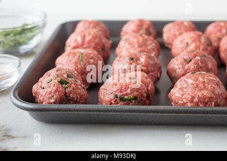 Boulettes de viande crus préparés et prêts à être cuits sur une feuille avec les assaisonnements sur le côté Banque D'Images