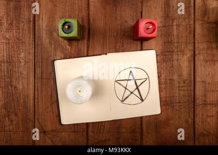 Une photo prise à la verticale de bougies et d'un grimoire, un livre de sorts, avec un pentacle dessiné à la main, tourné à partir de ci-dessus, sur un fond sombre avec un p Banque D'Images