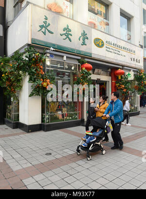 Une famille passe devant un magasin de médecine sur la rue Wangfujing à Beijing, Chine, décorée d'une profusion de fleurs artificielles d'affichage Banque D'Images