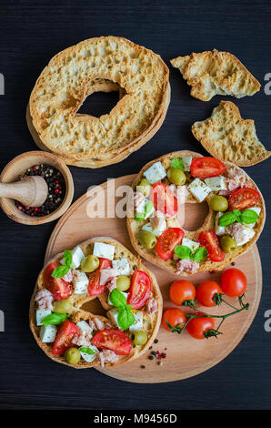 Frisella classique tomate, fromage mozzarella, thon et olives. Friselle démarreur italien. Pain séché appelé freselle sur planche de bois avec des tomates che Banque D'Images