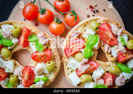 Frisella classique tomate, fromage mozzarella, thon et olives. Friselle démarreur italien. Pain séché appelé freselle sur planche de bois avec des tomates che Banque D'Images