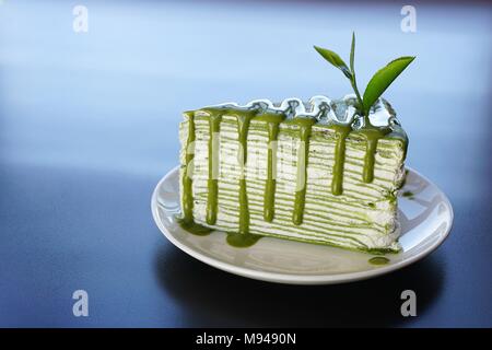 Morceau de gâteau crêpe au thé vert sur plaque blanche et décoré avec des feuilles de thé fraîches Banque D'Images