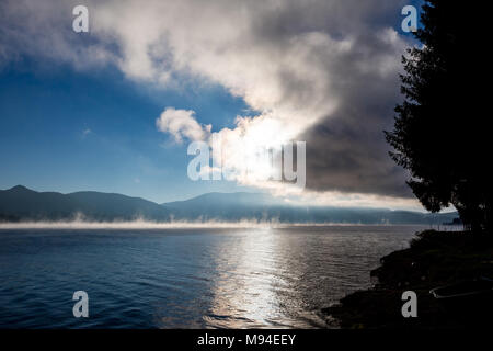 Soleil d'automne qui sort des nuages, reflets de lumière sur la surface du lac avec de l'eau evaporations au lac Dospat, Rhodopes, Bulgarie Banque D'Images