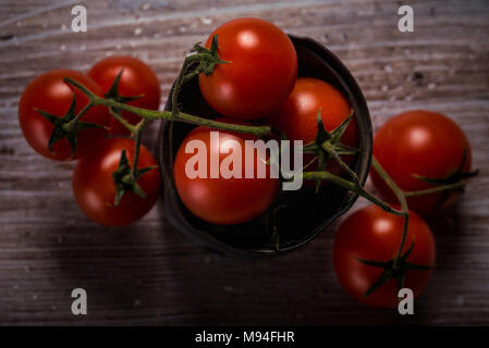 Photo horizontale avec vue de dessus sur plusieurs petites branches des petites tomates cerises rouges. Légume est placé dans de vieux métaux usés peuvent et sur pendentif en bois vintage Banque D'Images