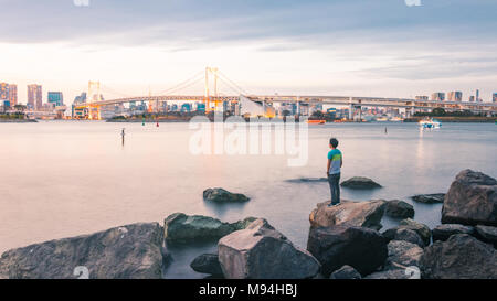 Un coucher de soleil panoramique vue sur le paysage urbain de Tokyo et l'emblématique pont en arc-en-ciel à partir de la station Odaiba Park Shore. Banque D'Images