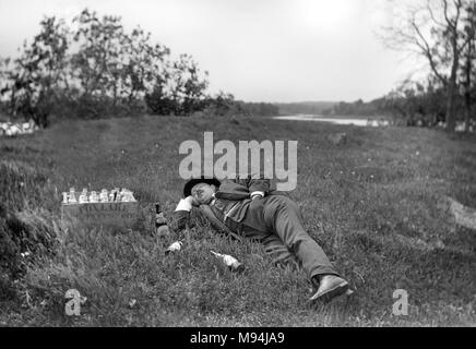 Un homme pose dans l'herbe qui peut accueillir une rencontre avec une caisse de bière de la brasserie de Fox Lake dans le Wisconsin, ca. 1905. Banque D'Images