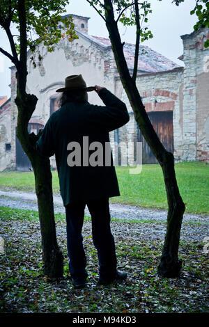 Cowboy debout derrière des arbres et en regardant l'ancienne ferme Banque D'Images