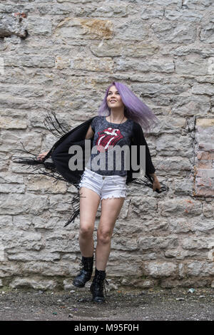 Modèle féminin blanc caucasien et brique pierre. Belle fille avec de longs cheveux violet reposant dans la ville, la mode moderne concept. Femme debout en face Banque D'Images