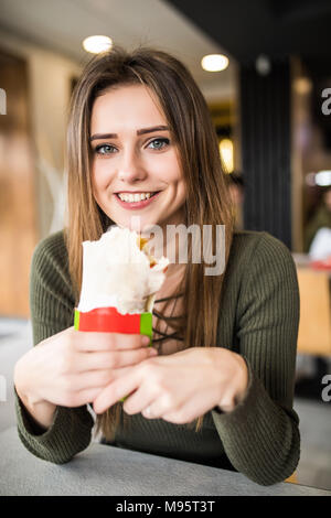 Jeune femme assise dans un restaurant manger un doner la main- la faim, la nourriture, repas Banque D'Images