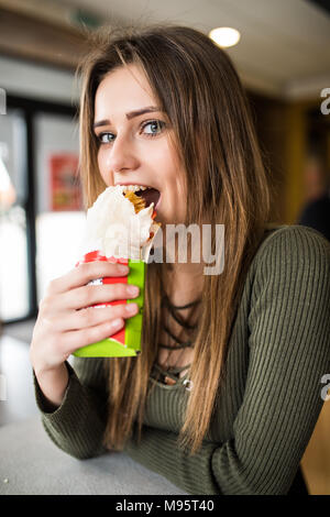 Jeune femme assise dans un restaurant manger un doner la main- la faim, la nourriture, repas Banque D'Images