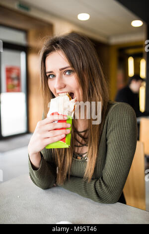 Jeune femme assise dans un restaurant manger un doner la main- la faim, la nourriture, repas Banque D'Images