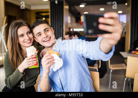 Femme heureuse et un bel homme profitent de leur délicieux et savoureux hamburgers et prise téléphone selfies doner Banque D'Images