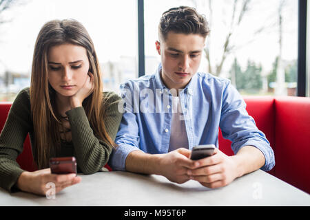 Phubbing, toujours connecté, la dépendance à internet, young couple in cafe à à leurs smartphones, social network concept Banque D'Images