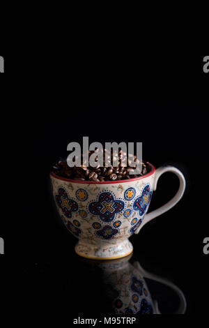 Une tasse remplie de grains de café est capturée par faible luminosité sur fond noir. Banque D'Images