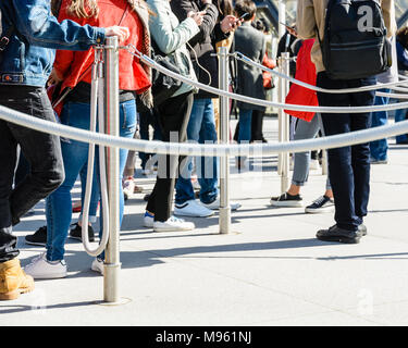 Les personnes se tenant dans la ligne entre les poteaux de file d'acier inoxydable gris avec des cordes, à l'entrée d'un site touristique, s'appuyant sur les pôles ou de regarder leurs Banque D'Images