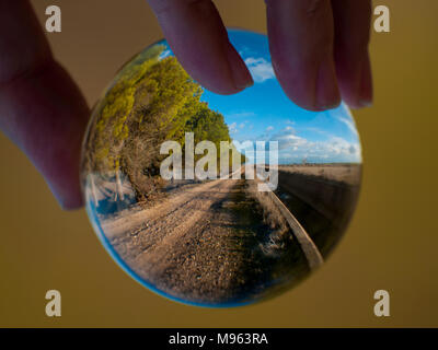 Woman hand holding bille de verre avec vue panoramique sur campagne et ciel bleu/ Concept pour l'environnement Banque D'Images