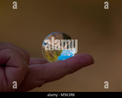 Woman hand holding bille de verre avec vue panoramique sur campagne et ciel bleu/ Concept pour l'environnement Banque D'Images