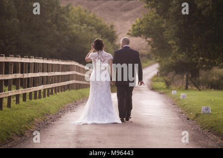 Couple nouvellement marié marche main dans la main vers le bas country lane Banque D'Images