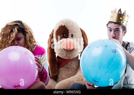Jeune femme avec man blowing balloons while sitting par gros chien en peluche Banque D'Images