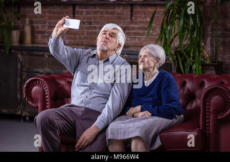 Young couple avec selfies smart phone while sitting on sofa at home Banque D'Images