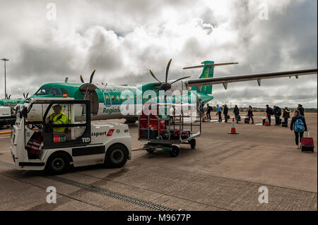 Les passagers embarquant dans un avion Aer Lingus ATR 72-600 de Cork à Birmingham en tant que gestionnaire de bagages entraîne un chariot avec des bagages à charger dans la soute. Banque D'Images