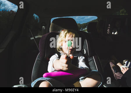 Fille avec une sucette verte sitting in car seat Banque D'Images