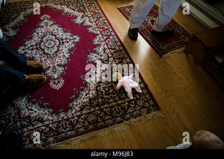 Baby doll portant sur un tapis avec d'autres personnes debout autour d'elle Banque D'Images