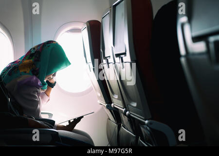 Femme musulmane solitaire voyageant en avion lors de la lecture sur les sièges lors d'un coucher de soleil, mode ambiance lowlight Banque D'Images