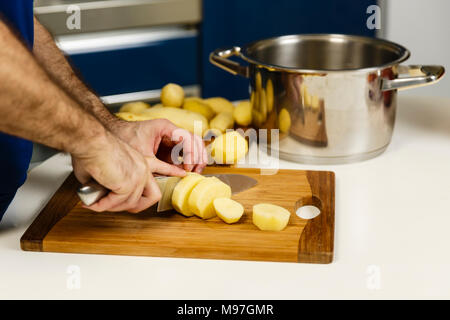 Gros plan du man's hands slicing raw les pommes de terre sur une planche en bois Banque D'Images