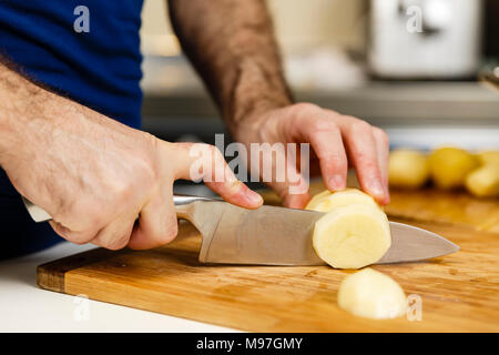 Gros plan du man's hands slicing raw les pommes de terre sur une planche en bois Banque D'Images