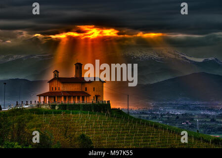 Un faisceau de lumière filtre à travers les nuages orageux et semble s'allumer la chapelle du partisan de culte de Bastia Mondovì, les Langhe, Piémont, Italie. Banque D'Images