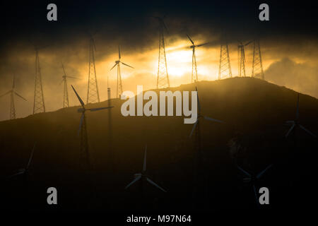 L'analyse des nuages au sommet d'une colline et alors que le soleil se couche sur une ferme éolienne, Tarifa, Espagne Banque D'Images