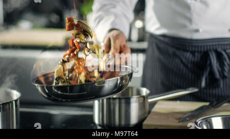 Chef cuisine de style professionnel flambe. Il prépare le moule dans une casserole avec des flammes. Il travaille dans une cuisine moderne avec différents ingrédients qui traînent Banque D'Images