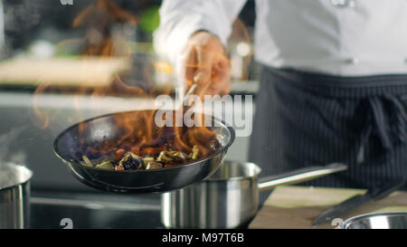 Chef cuisine de style professionnel flambe. Il prépare le moule dans une casserole avec des flammes. Il travaille dans une cuisine moderne avec différents ingrédients qui traînent Banque D'Images