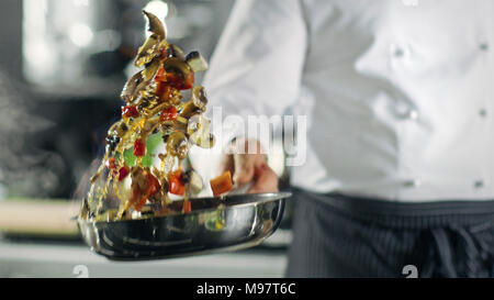 Chef cuisine de style professionnel flambe. Il prépare le moule dans une casserole avec des flammes. Il travaille dans une cuisine moderne avec différents ingrédients qui traînent Banque D'Images