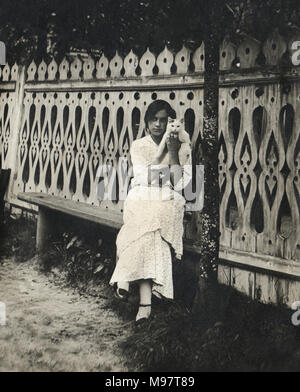 Vintage photo de la jeune fille avec un chat assis sur un banc près de la clôture en bois avec un joli motif taillé, Russie, 1914 Banque D'Images