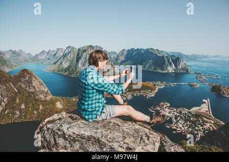 L'homme à l'aide de voyageurs assis sur smartphone falaise vie Voyage aventure concept piscine vacances d'été en Norvège montagnes vue aérienne Lofote Banque D'Images