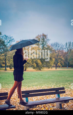 Jeune femme avec parapluie en équilibre sur deux bancs de parc d'automne Banque D'Images