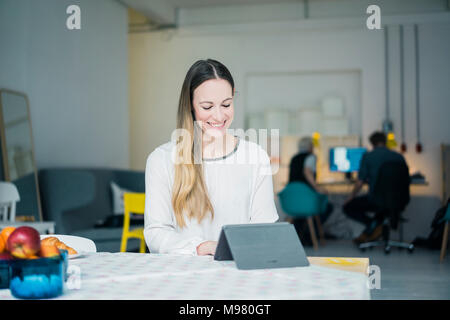 Portrait of smiling young businesswoman working on comprimé dans un loft Banque D'Images